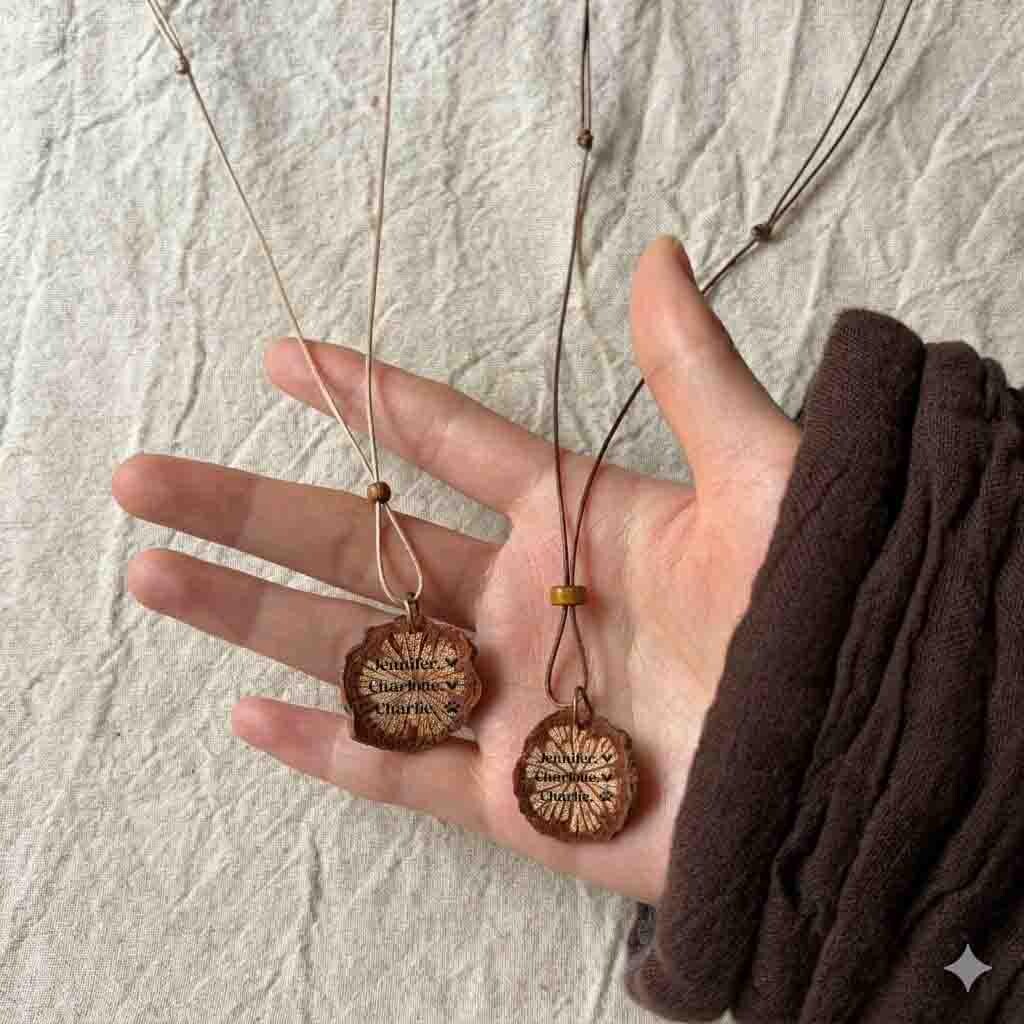 May include: Two necklaces featuring circular, natural wood slice pendants suspended on thin cords. Each pendant is engraved with the names Jennifer, Charlotte, and Charlie, accompanied by small heart and paw print symbols, showcasing a rustic aesthetic.