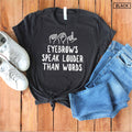 May include: Black t-shirt with white text that reads "Eyebrows speak louder than words". The text is accompanied by three hand gestures in American Sign Language. The shirt is laid out on a wooden surface with a pair of white sneakers and blue jeans.